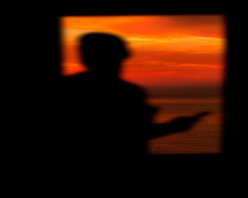 Mature person looking thoughtfully out a large window during sunset